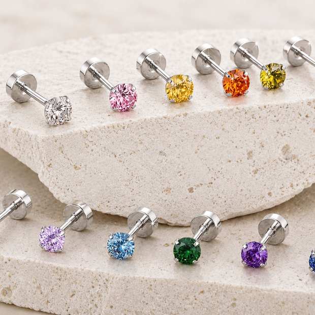 A set of colorful round stud earrings with silver posts and backing, displayed on textured stone slabs. The studs feature various gemstone colors including clear, pink, yellow, orange, green, red, light blue, purple, and dark blue.