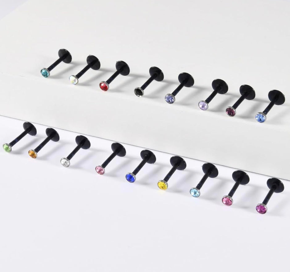 Twelve black labret-style body jewelry piercings with faceted gemstone tips in various colors, arranged in two rows on a clean white background.