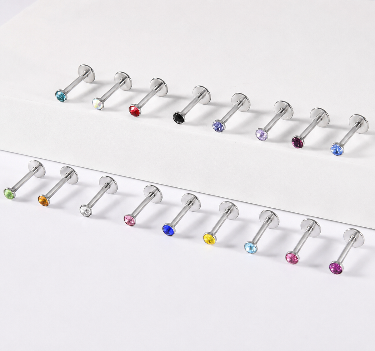 Two horizontal rows of silver-toned labret piercings with faceted gemstone backings in assorted colors, arranged on a clean white background.