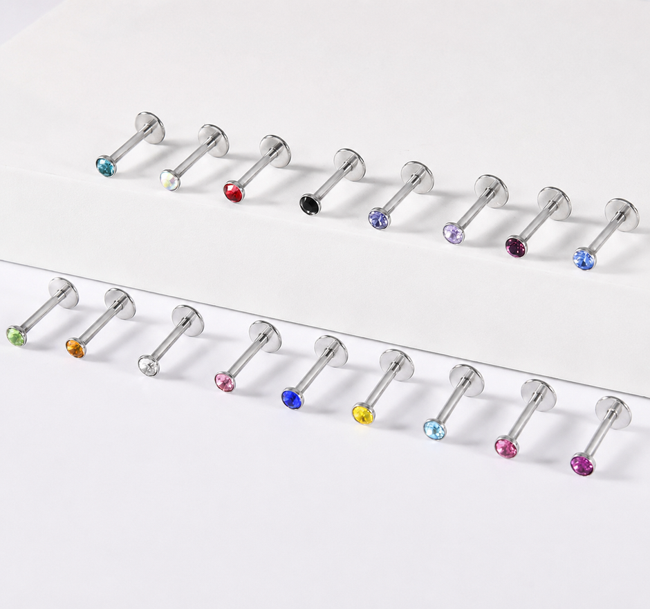 Two horizontal rows of silver-toned labret piercings with faceted gemstone backings in assorted colors, arranged on a clean white background.