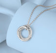 A silver-toned necklace with a double interlocking ring pendant, accented with small clear stones along one of the rings, displayed on a light blue jewelry bust.