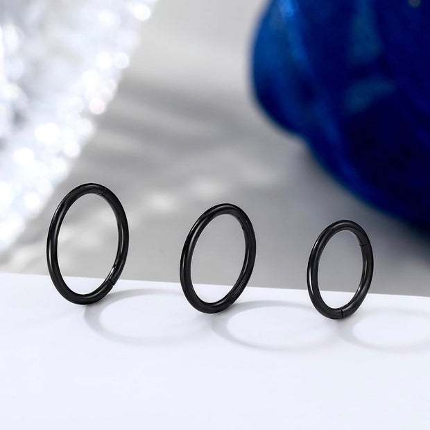 Three black metal O-ring style rings of varying sizes standing upright on a white surface, with a blurred blue and white background.