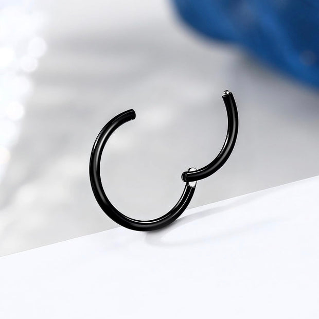 A single black metal hoop earring with a unique asymmetrical twist closure, resting on a white surface with a soft, blurred blue background.