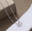 A silver chain necklace with a small, polished oval pendant resting on a white textured surface next to a brown box.