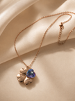 A rose gold chain necklace featuring a four-leaf clover pendant with three heart-shaped leaves engraved with 'LOVE', 'HATE', and 'PASSION', alongside a central purple heart-shaped crystal pendant, displayed on draped beige satin fabric.