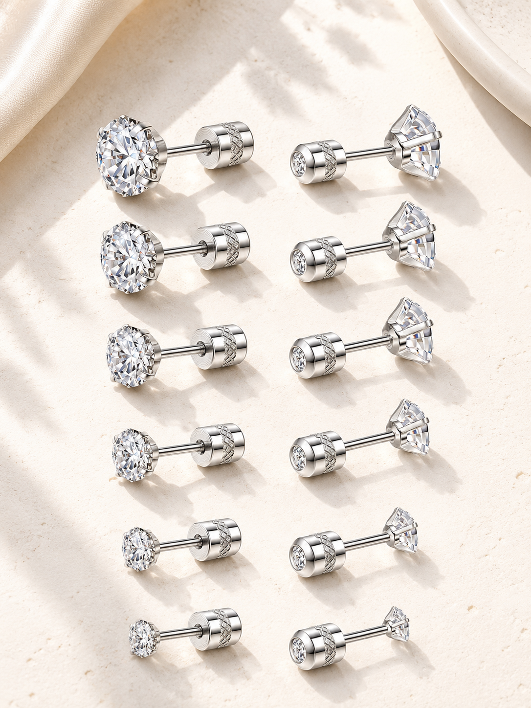 Twelve silver-toned labret stud earrings arranged in two columns on a light beige textured surface. Each earring has a clear gemstone set in different shapes including round, oval, pear, and marquise cuts.