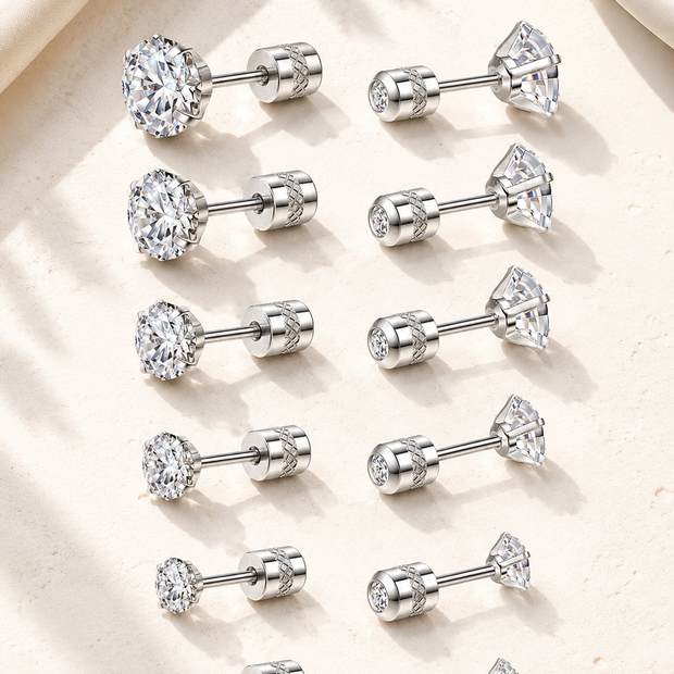 Twelve silver-toned labret stud earrings arranged in two columns on a light beige textured surface. Each earring has a clear gemstone set in different shapes including round, oval, pear, and marquise cuts.