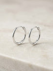 A pair of polished silver hoop earrings resting on a light beige stone surface.