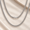 Two silver-toned curb chain necklaces draped elegantly on a beige satin fabric background.