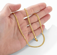 Gold chain held in a hand against a white background